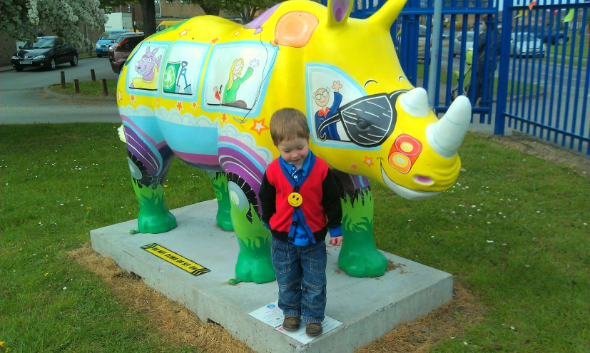 a little boy standing next to a statue of a rhino