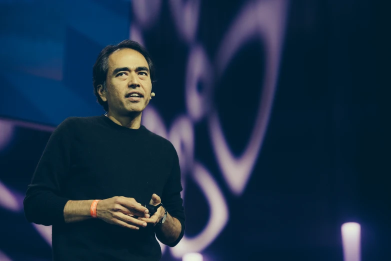 a man stands in front of a large screen and speaks