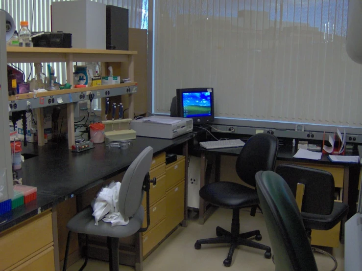 some sort of office with black chairs and laptop on the desk