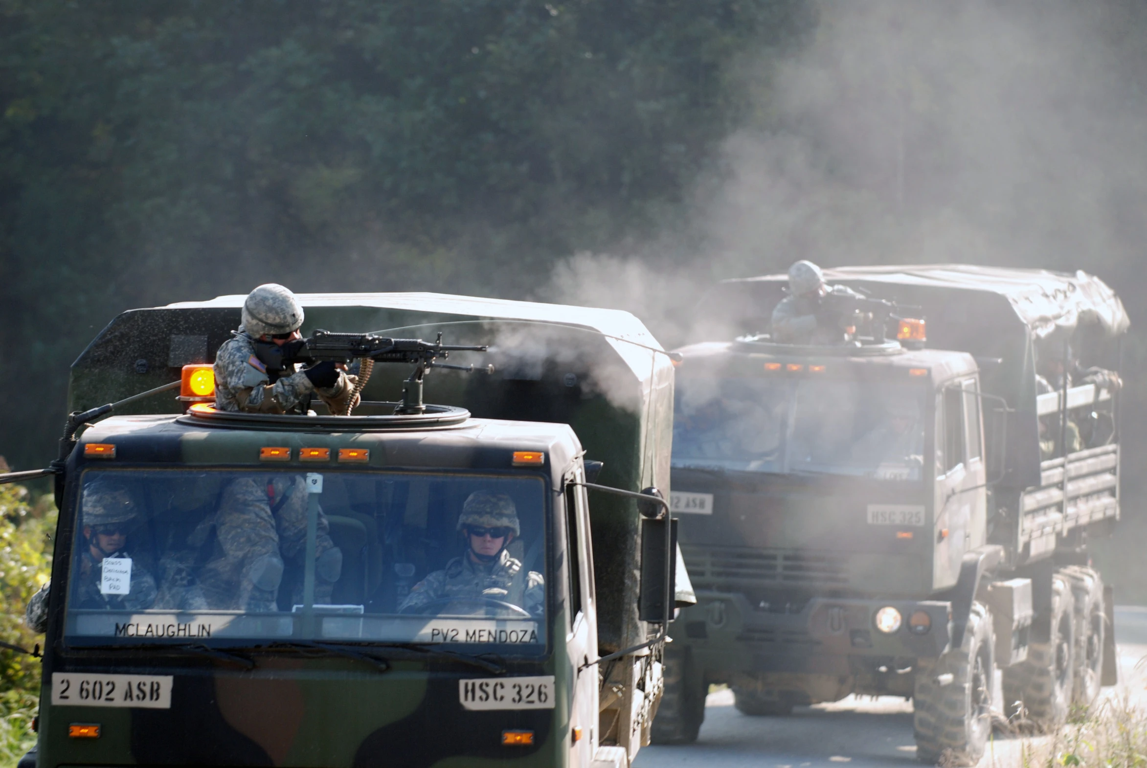 two military trucks moving down a country road