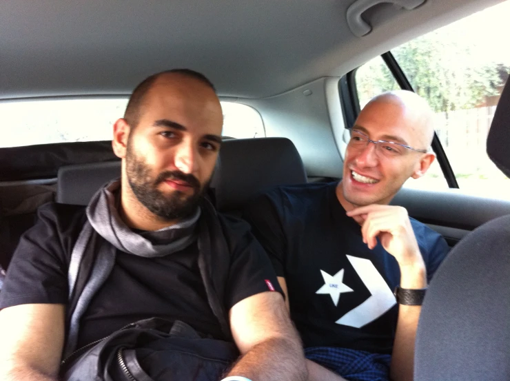 two men smiling in the back seat of a car