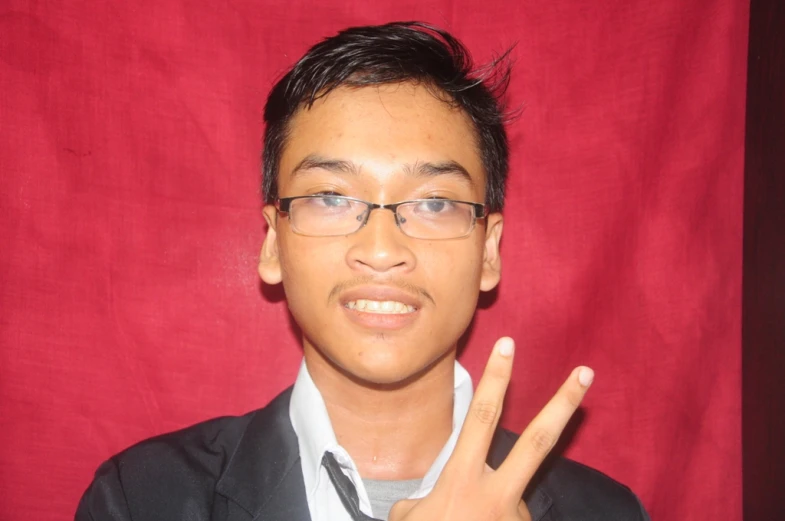 young man wearing glasses standing in front of a red background