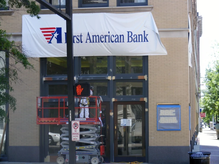 man on top of scissor working in front of bank building