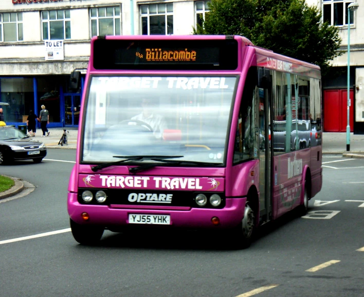 a pink passenger bus driving down a street