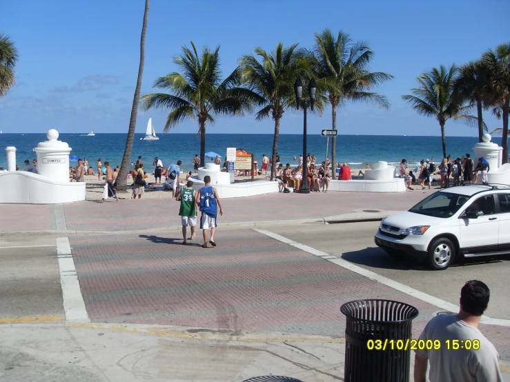 people walking across a busy city street near a body of water