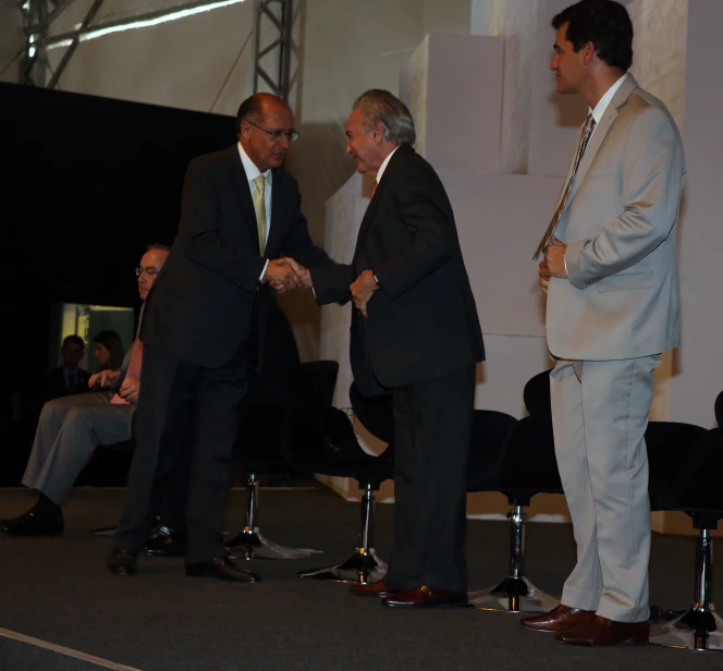 two men in suits shaking hands at a stage