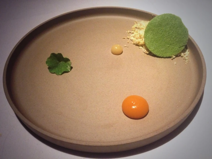 green food on a plate with a shell, a yellow egg and other small vegetables