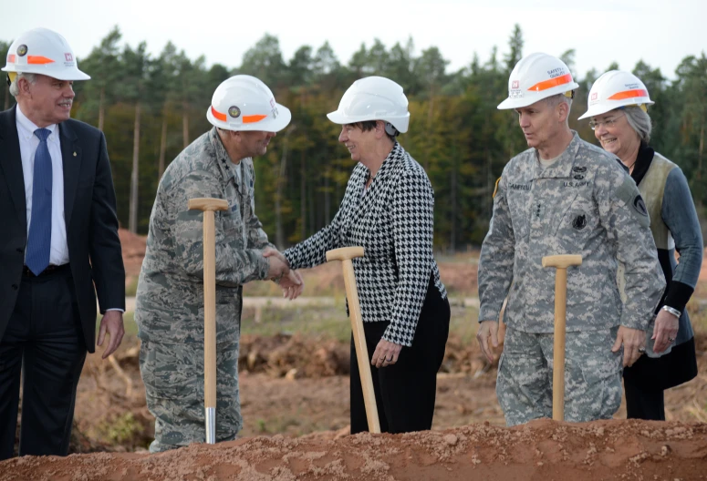 three men and two women holding shovels together in front of trees