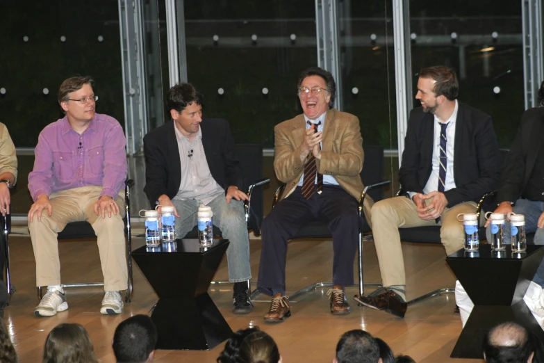 five men talking on stage while sitting next to each other