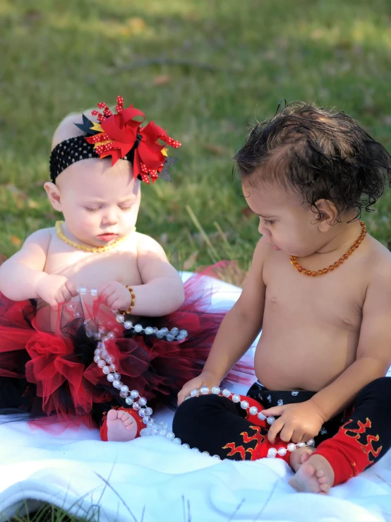 a small baby sitting on a blanket next to an infant on the ground