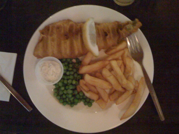 a plate has fried fish and green peas with a knife