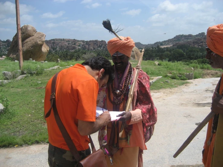 men in orange shirt with some sticks and a bag