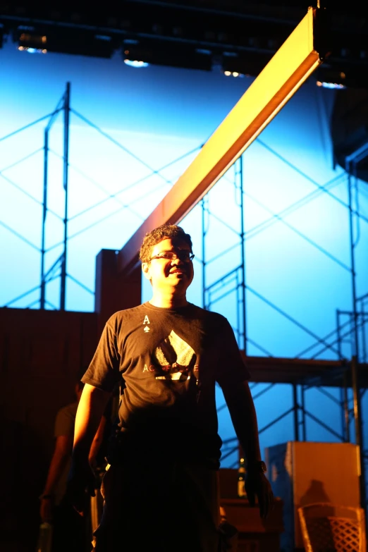 a man holding a giant wooden sign in front of blue lit scaffolding