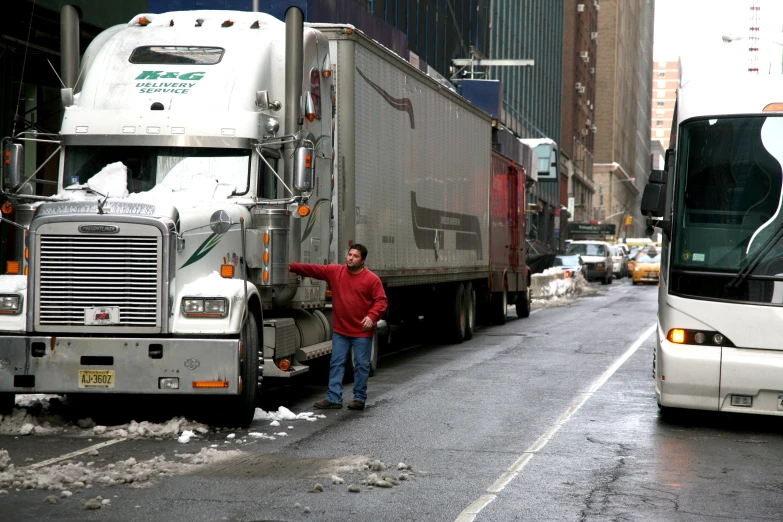 a large truck parked in the middle of a road with it's driver standing on the sidewalk