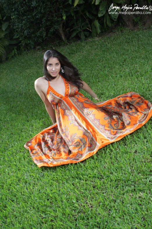 a beautiful woman laying in the grass wearing an orange and black dress