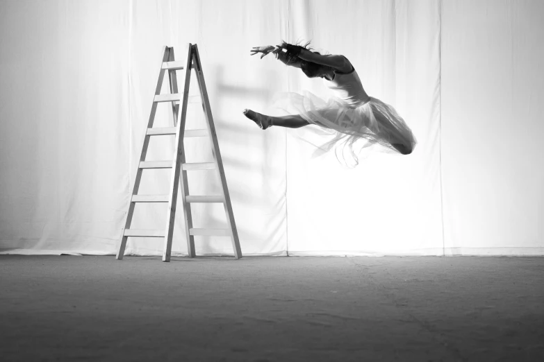 woman in ballet dress doing a split on a stage next to a ladder