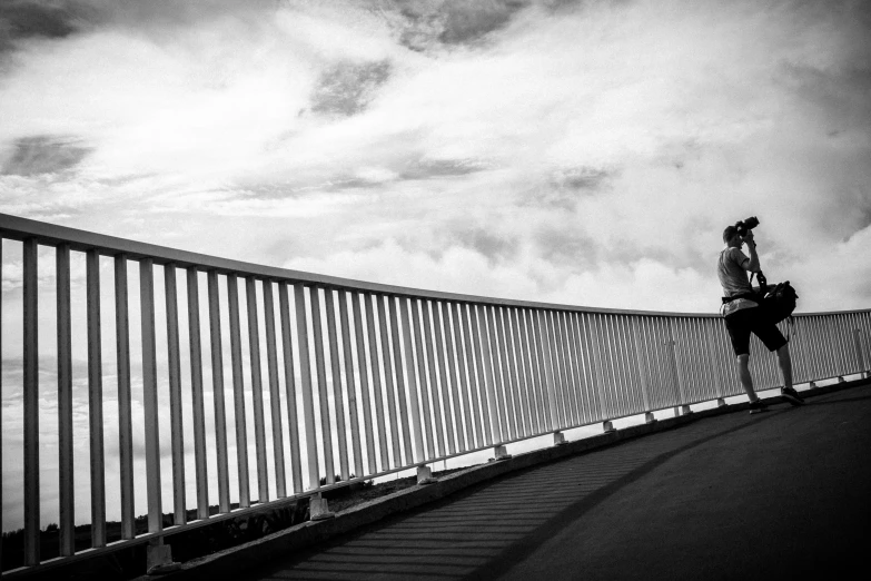 man riding his skateboard on a bridge against the clouds