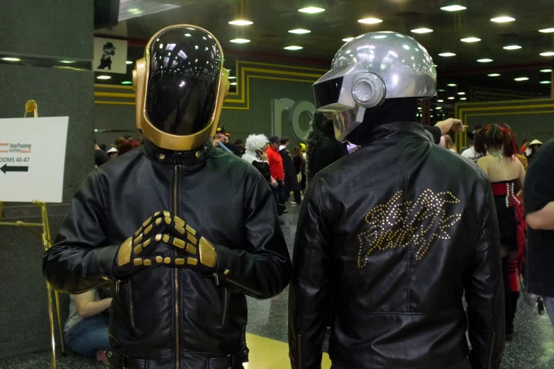 two men wearing black and gold jackets standing in front of an elevator