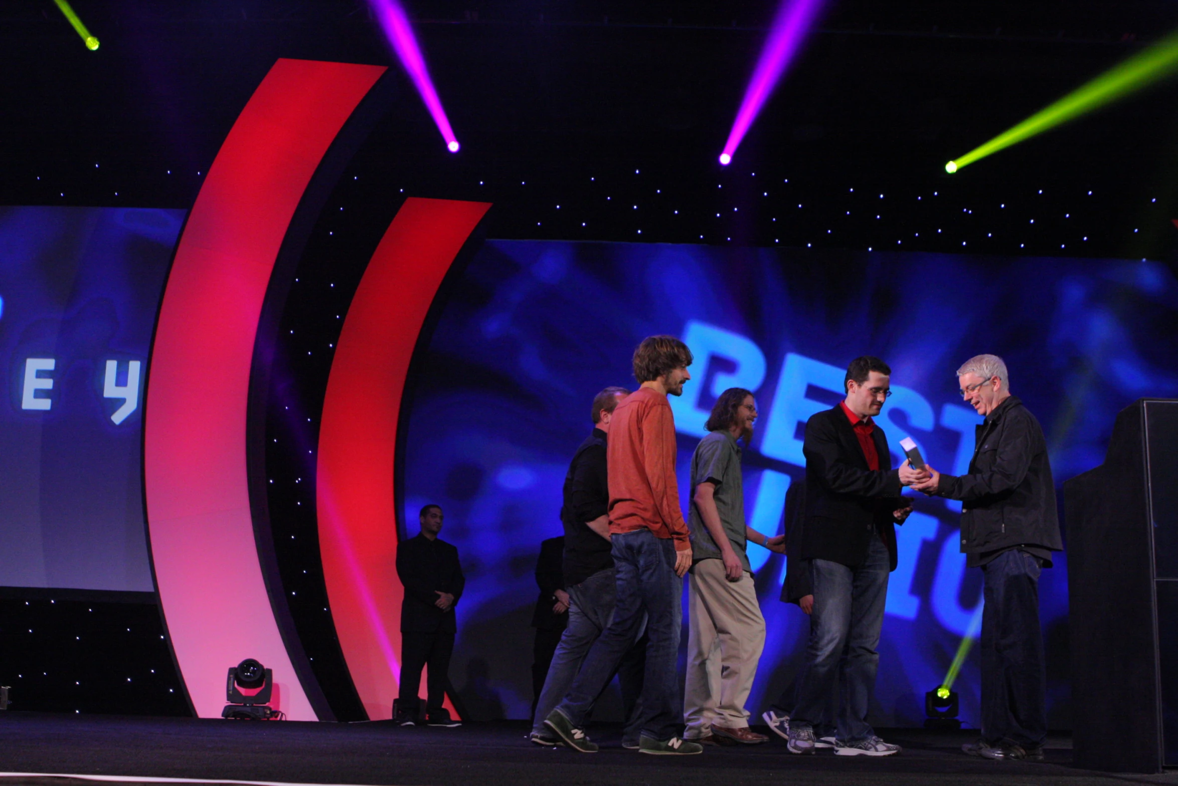 four people stand on stage looking at a device