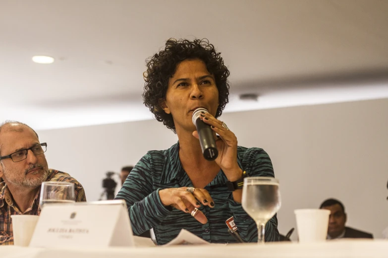 a woman speaking into a microphone in front of a group of people