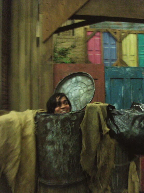 a young person peeking into the camera behind a metal bucket