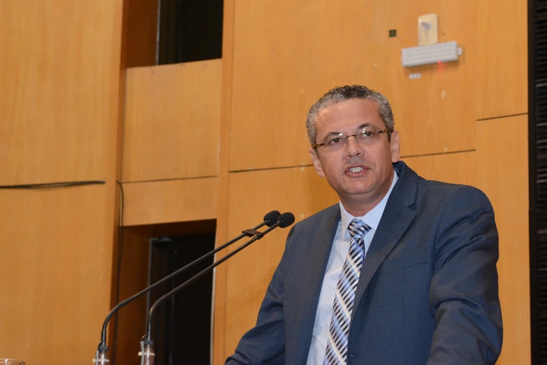 a man standing at a podium holding a drink