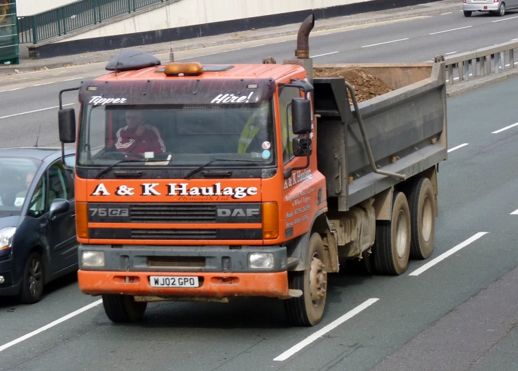 an orange truck is driving by a black car