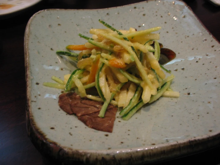 a square white plate topped with pasta and vegetables