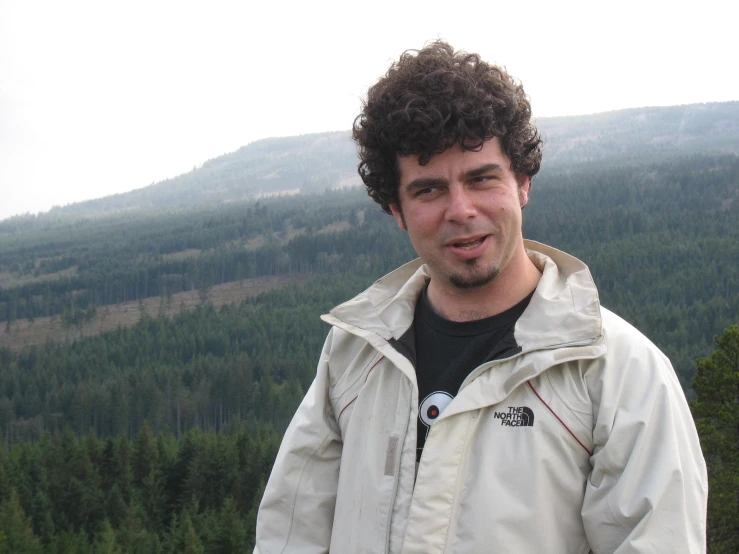 a man in a parka stands near some trees