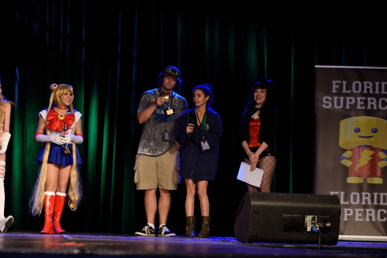 several people on stage talking and wearing costumes