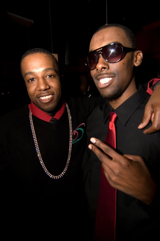 two guys with sunglasses and one in a shirt and red tie posing for a camera