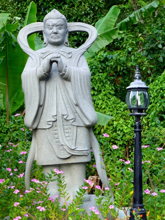 statue sitting on top of cement surrounded by flowers