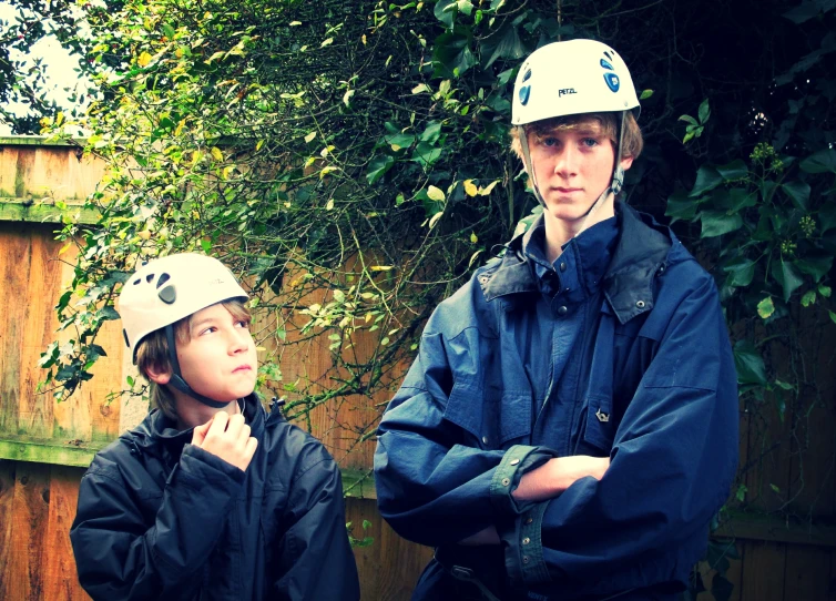 two boys standing together, with helmets on and one boy in raincoat