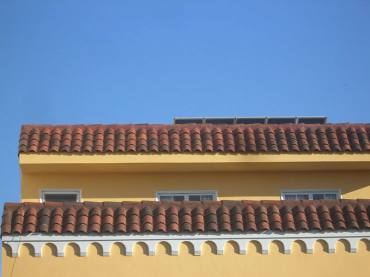 the top of a roof with arched, open windows and an orange building with an open sky background