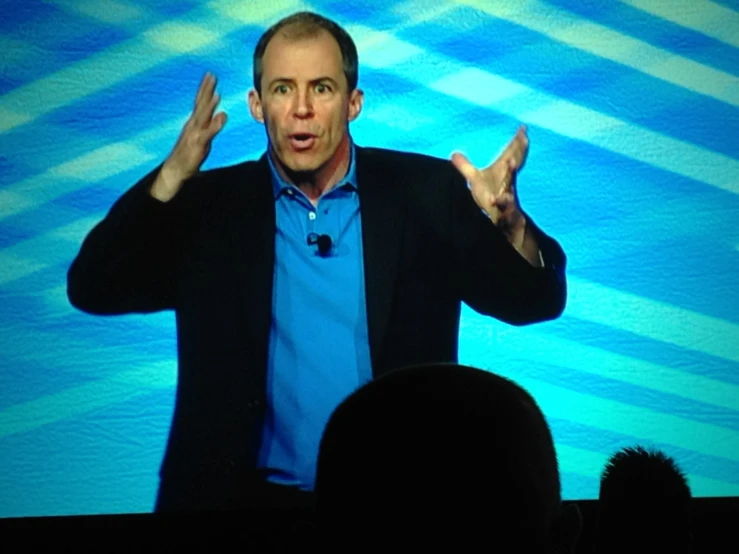 a man in a blue shirt and jacket speaking on stage