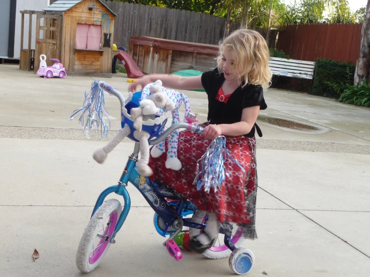 a girl riding on a blue bike with a toy dog on the back of it