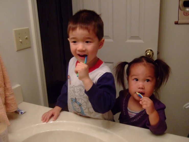 a couple of children brushing their teeth in the bathroom