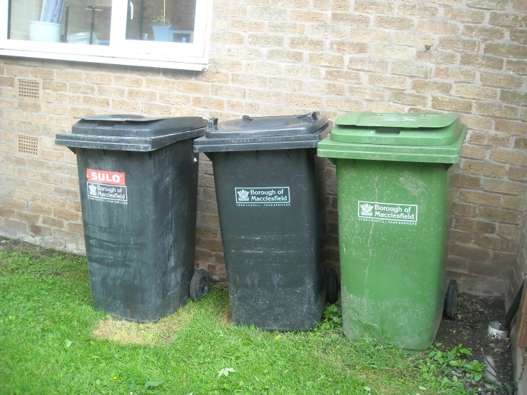 three trash cans are placed beside a wall