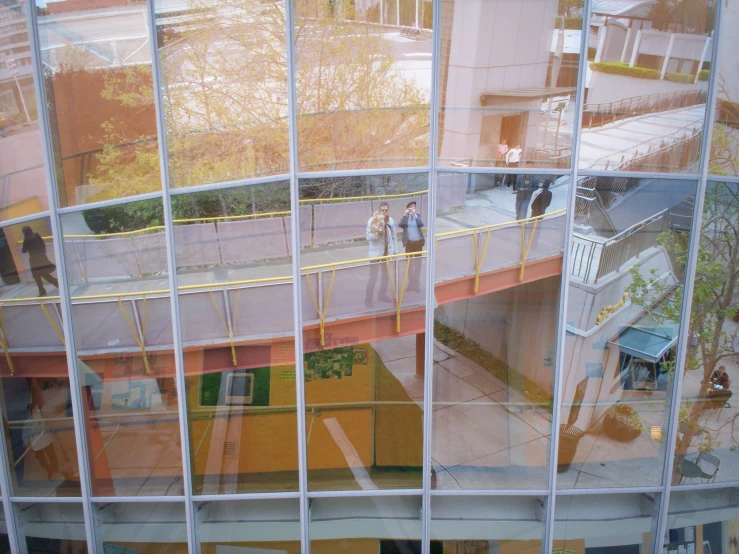 the inside of a building that has people on a bridge and buildings as seen through large windows