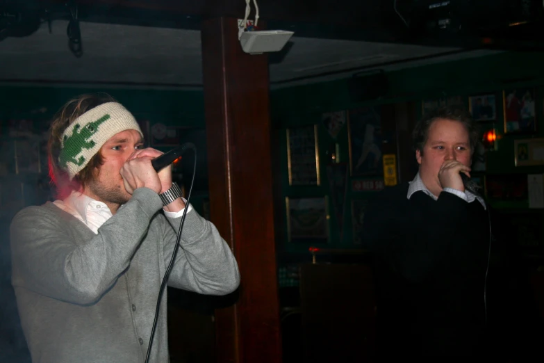 two young men singing with microphones in a bar