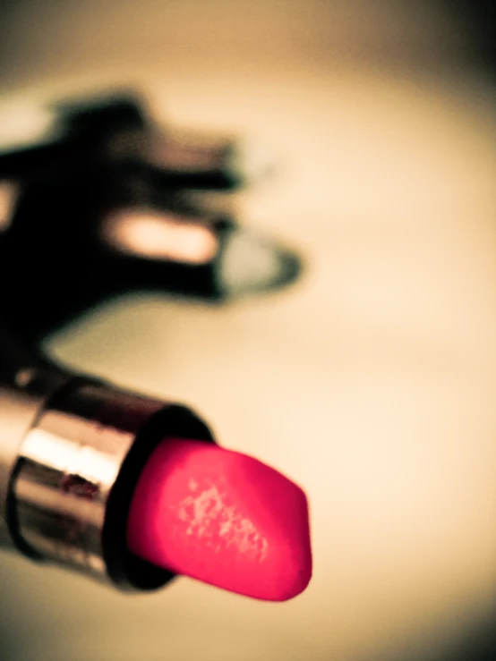 a pink lipstick bottle sitting next to a pair of silver metal scissors