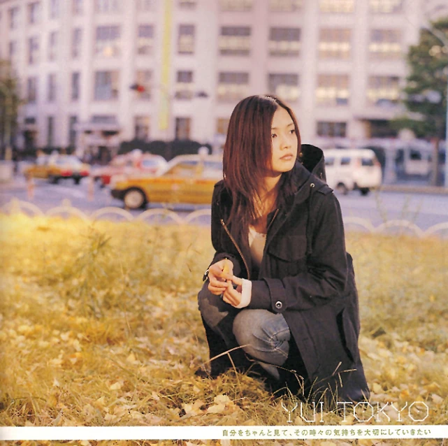 woman sitting in grassy area near buildings and cars