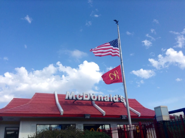 an american flag flies in front of a mcdonald's with a sky background