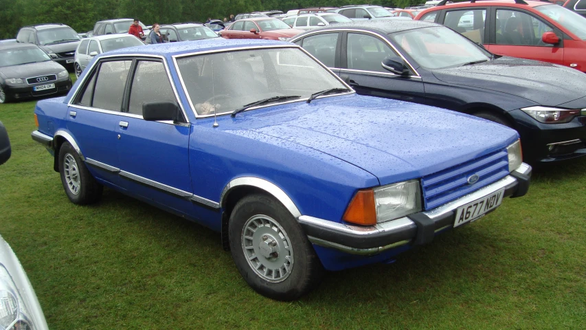 a blue, older model car is parked in a lot