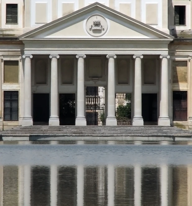 the front of an old building with columns, windows and some water