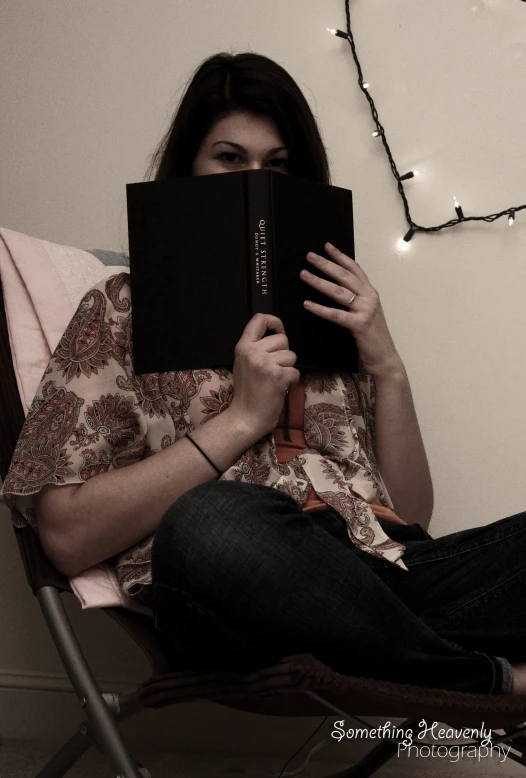 a woman sits in a chair with a book over her mouth