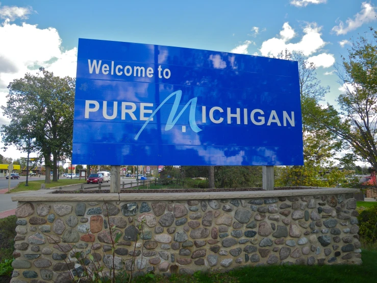 a large welcome sign with a blue signboard is near a brick wall