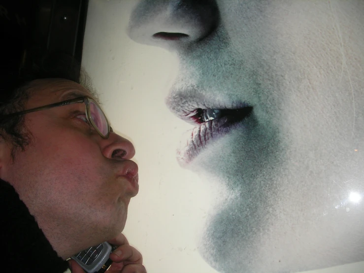 a close up of a man with a cell phone near a large poster