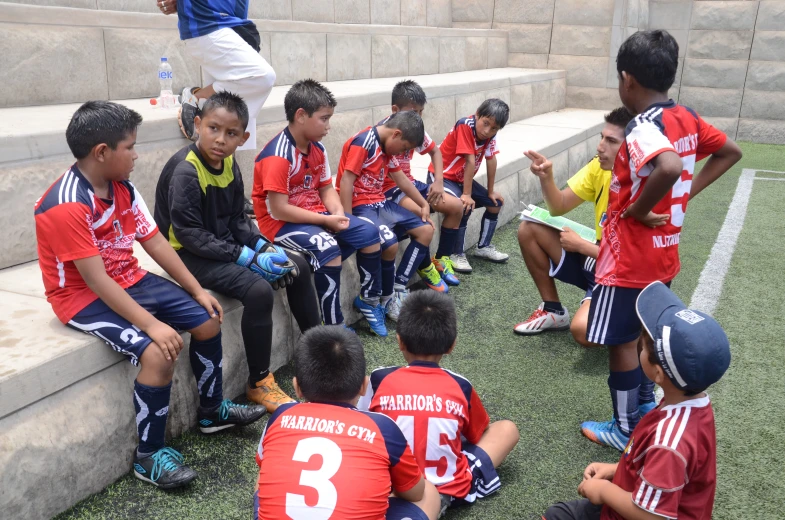 a bunch of children wearing matching jerseys sitting on the side walk