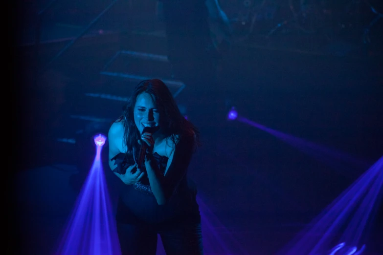 a woman standing at a microphone in front of purple light beams